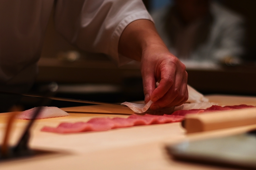 Sushi chef thinly slicing raw fish