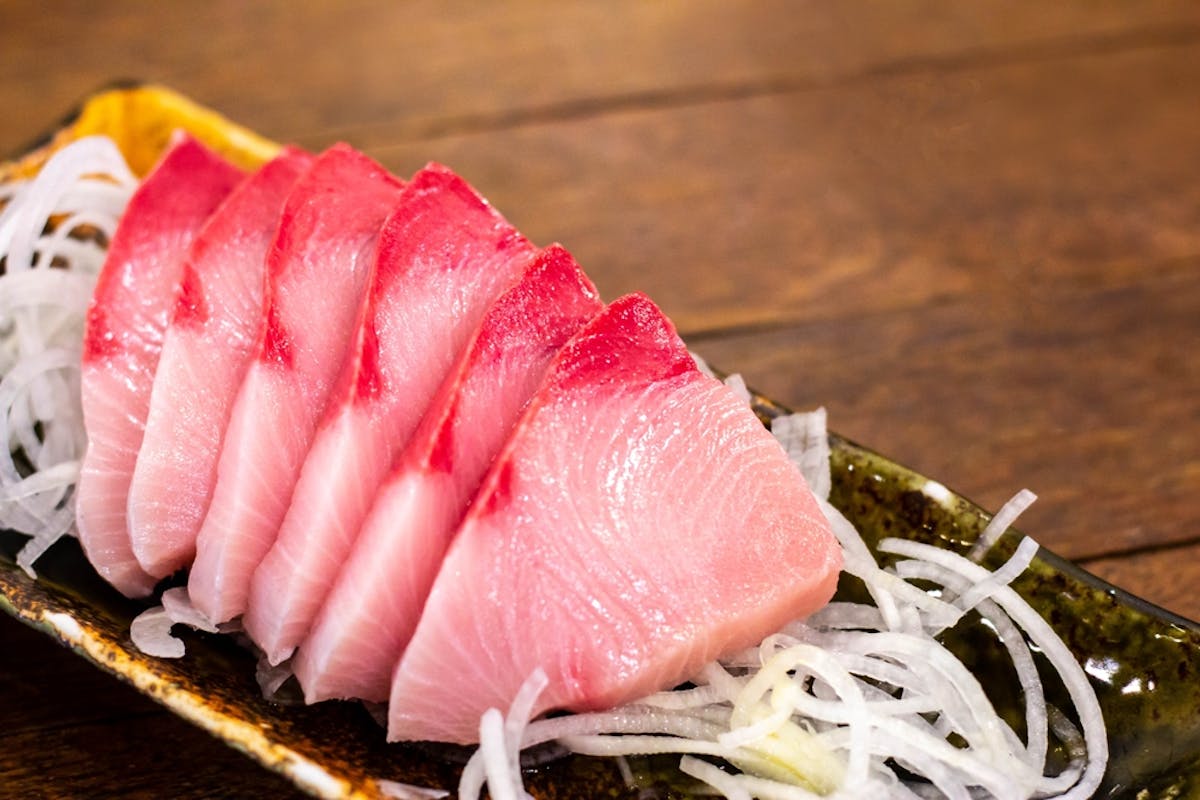 Hamachi yellowtail on a black dish on a wooden table