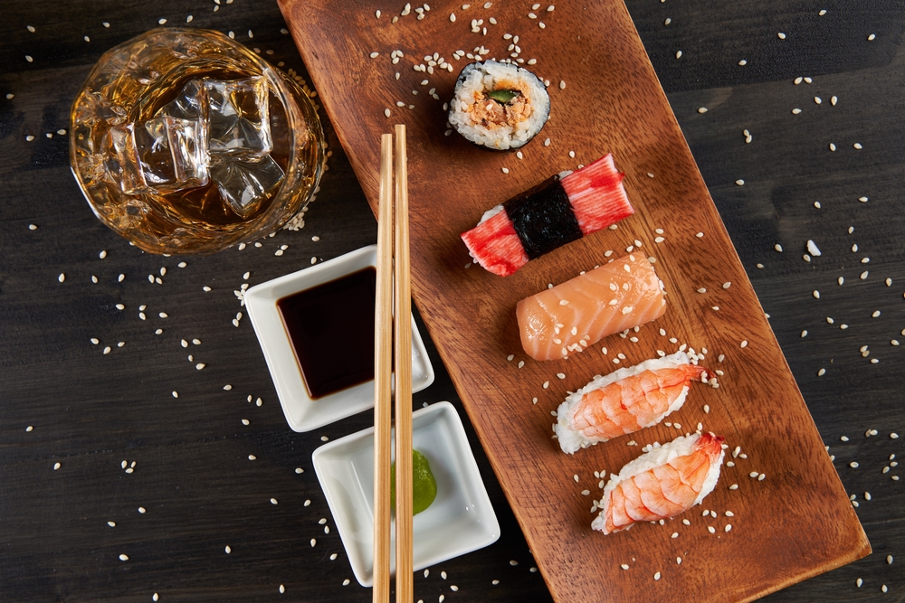 glass of whiskey with various sushi options on wood with soy sauce and wasabi sauce