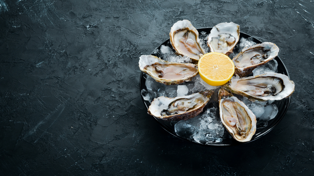 Seven freshly shucked oysters on a tray with lemon