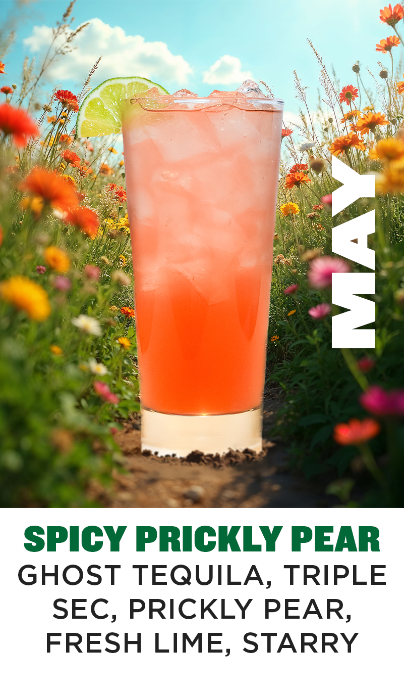 a glass of orange liquid in a field of flowers