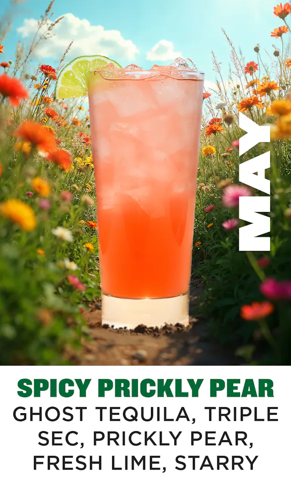 a glass of orange liquid in a field of flowers
