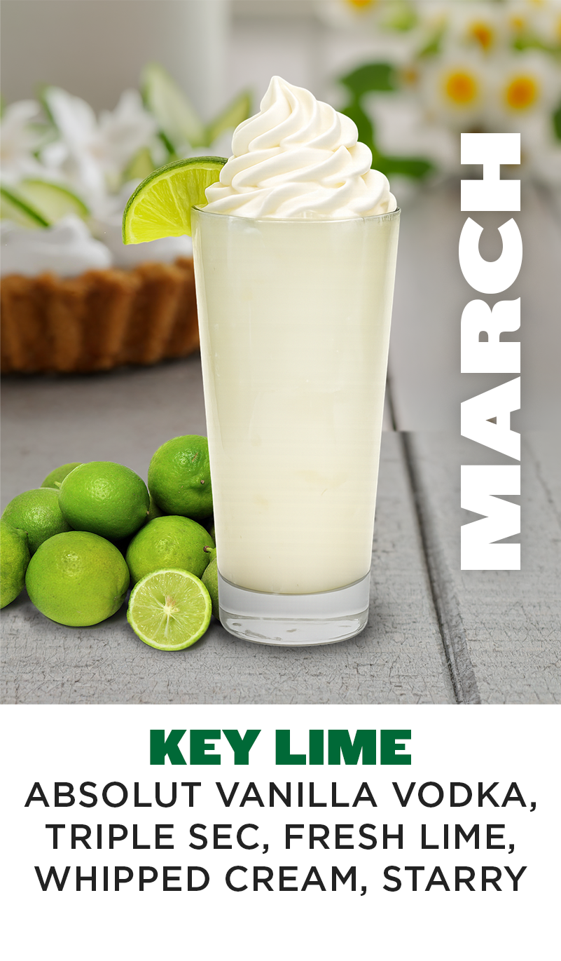 a glass of white liquid with a lime wedge and a few limes