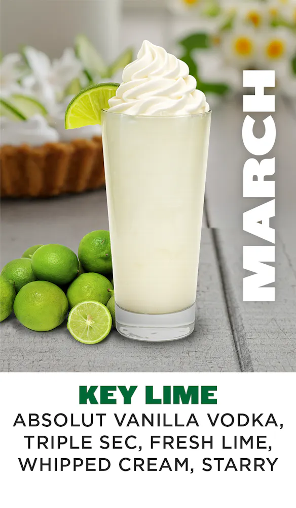 a glass of white liquid with a lime wedge and a few limes