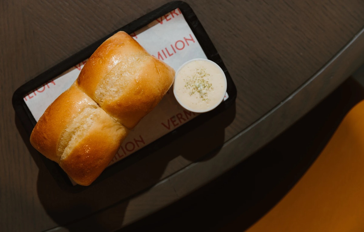 Soft dinner rolls served with creamy dipping sauce on a black tray.