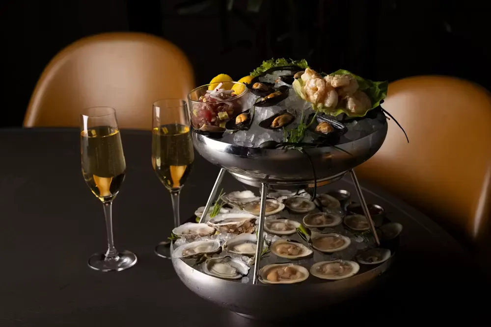Tiered seafood platter with fresh oysters, clams, mussels, and shrimp on ice, served with two glasses of champagne.