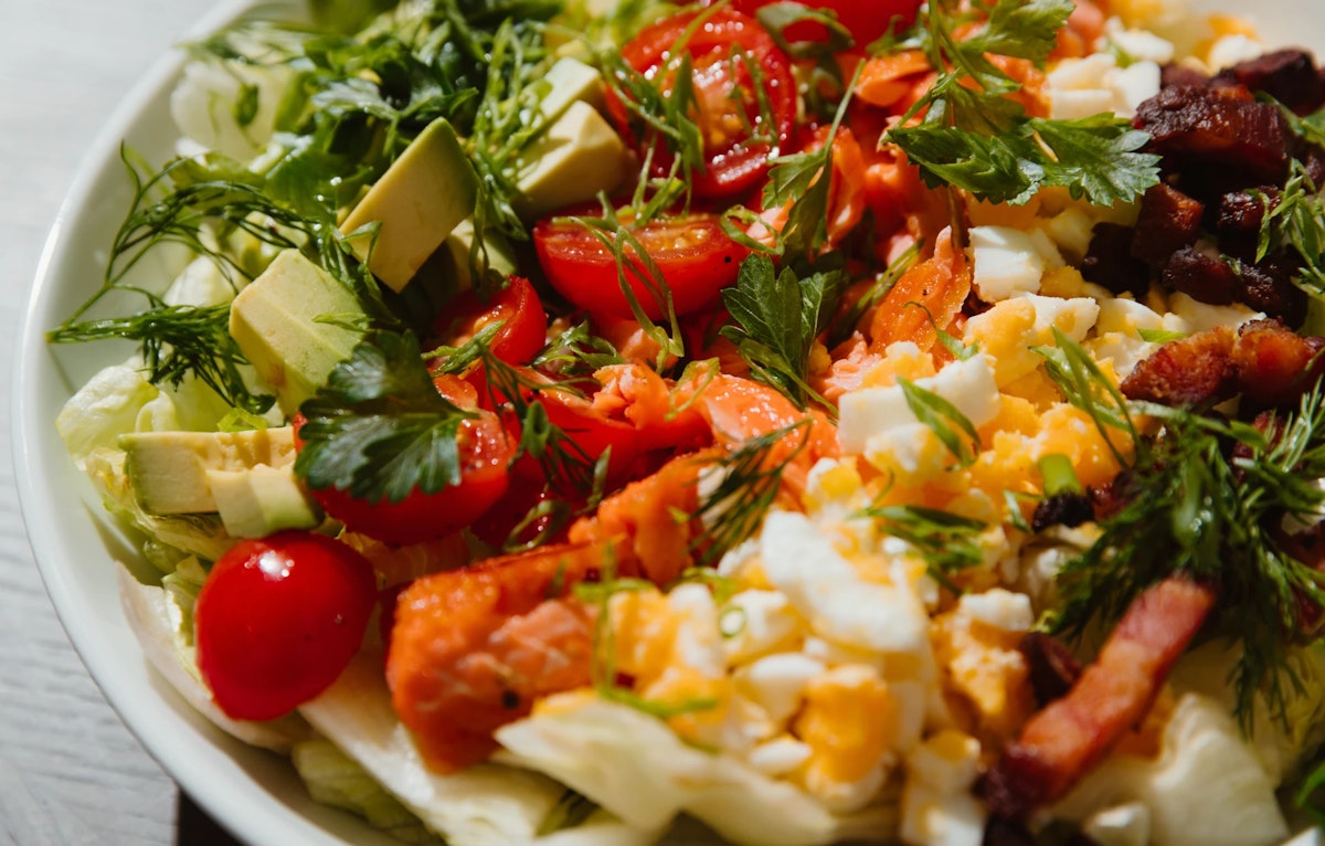Bowl with lettuce, tomato, avocado, boiled egg, salmon and bacon