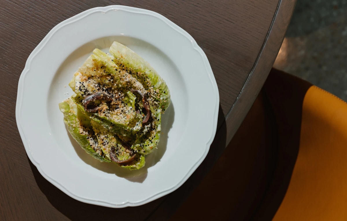 Romaine lettuce salad with anchovies, grated cheese, and seasoning on a white plate.