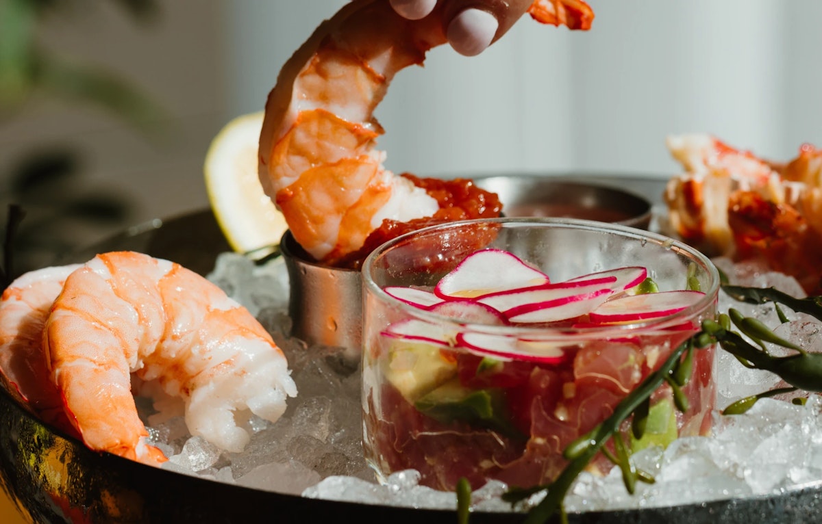 Shrimp cocktail with radish and avocado served on crushed ice with cocktail sauce.