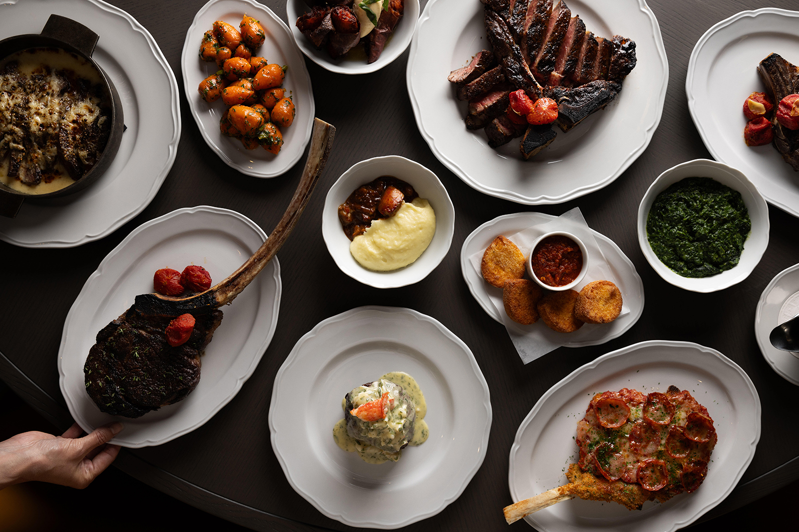 Prime 850 dry-aged steaks and assorted dishes including mashed potatoes, carrots, and croquettes on a table.
