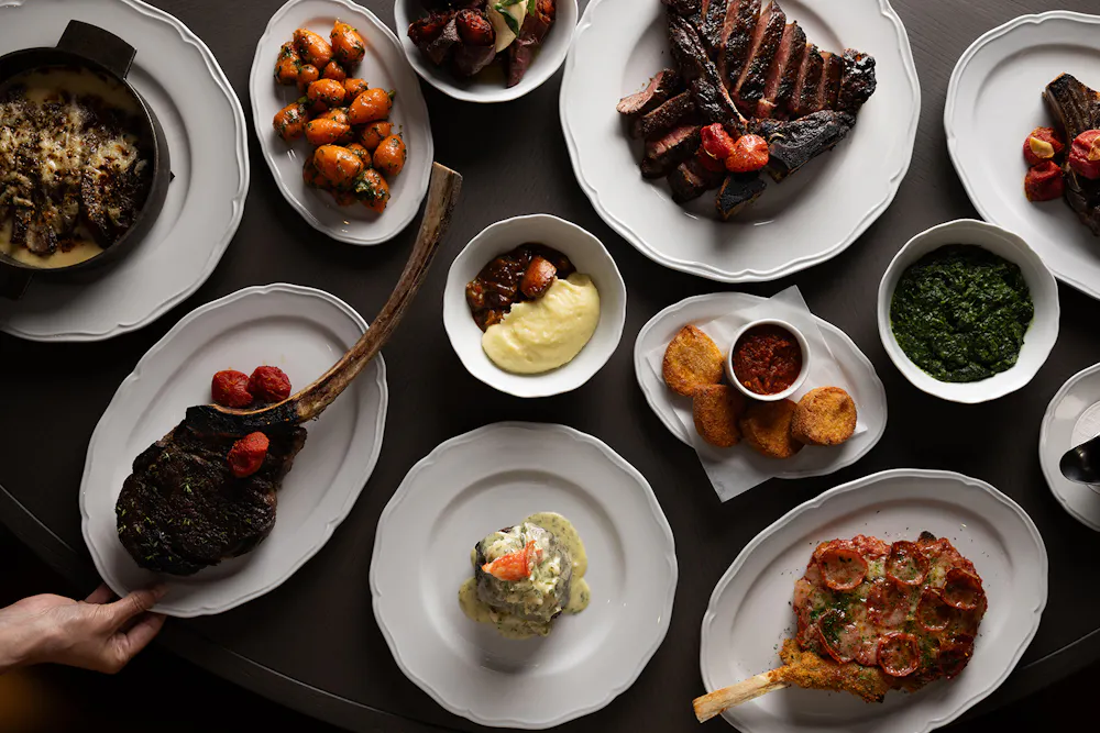 Prime 850 dry-aged steaks and assorted dishes including mashed potatoes, carrots, and croquettes on a table.