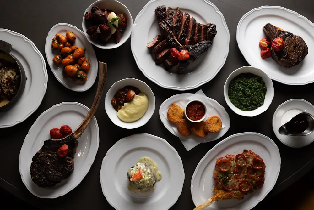 Assorted steak cuts, sauces, and sides arranged on a dining table before pairing wine with steak.