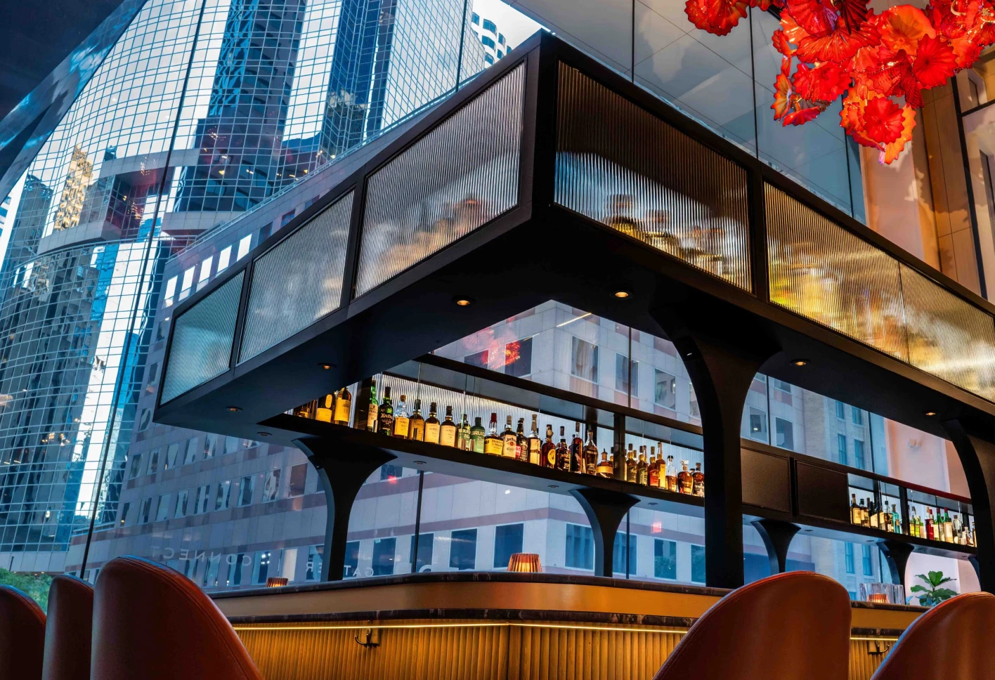The Vermilion Club bar beneath the Chihuly sculpture with city reflections.