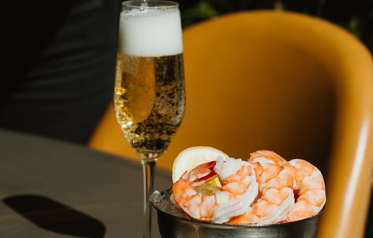 Chilled shrimp cocktail served with lemon slice and a glass of sparkling wine.