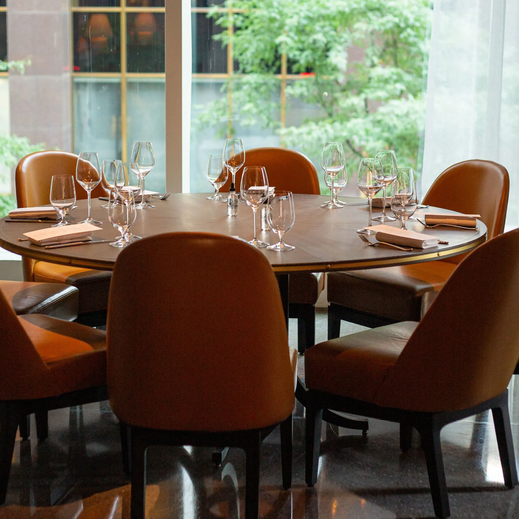Private dining room at The Vermilion Club, featuring a rectangular table with cutttlery, glasses, and warm amber lighting, with a red glass sculpture and bar area in the background.