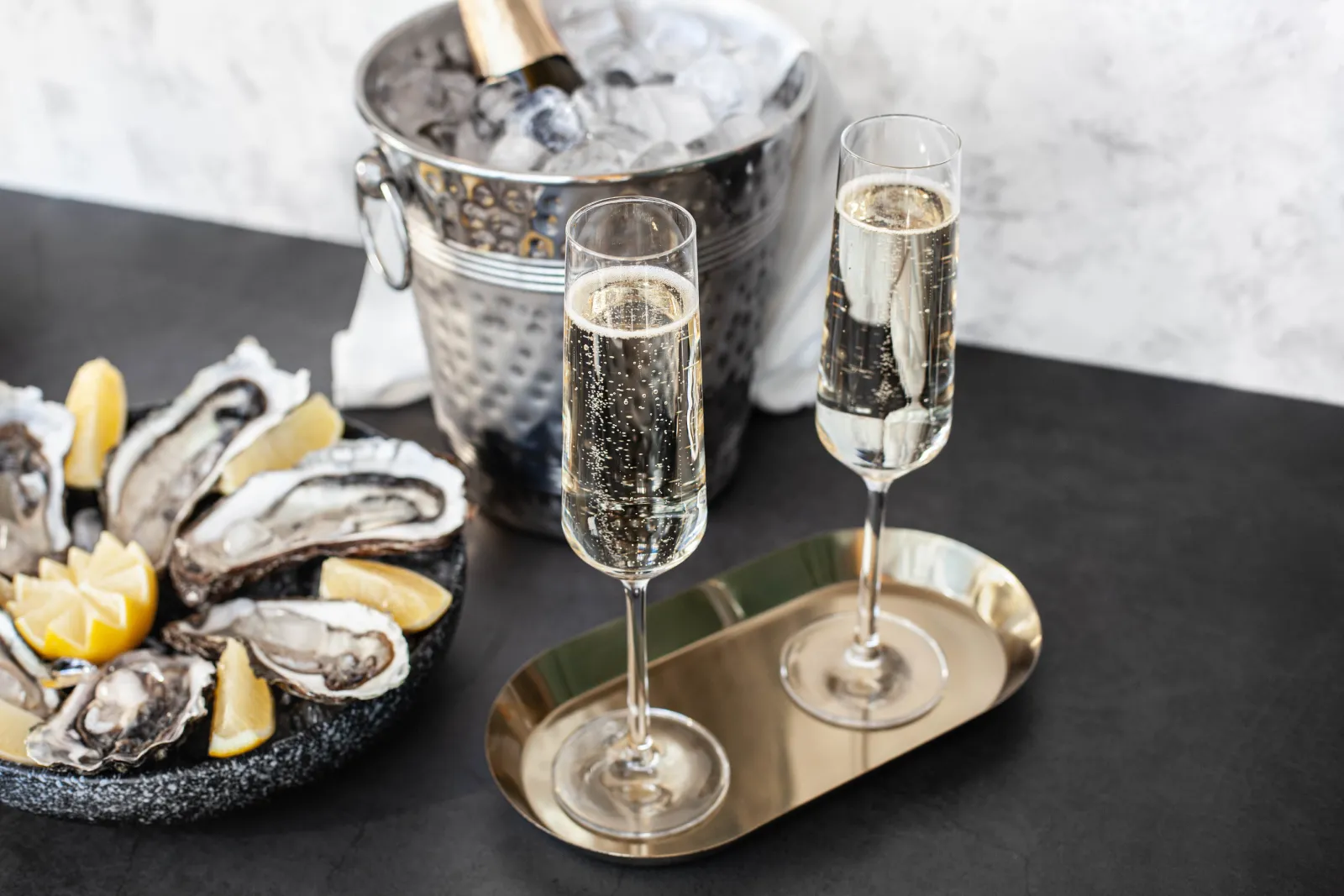 Fresh oysters with lemon wedges served alongside two glasses of champagne and an ice bucket with chilled sparkling wine.