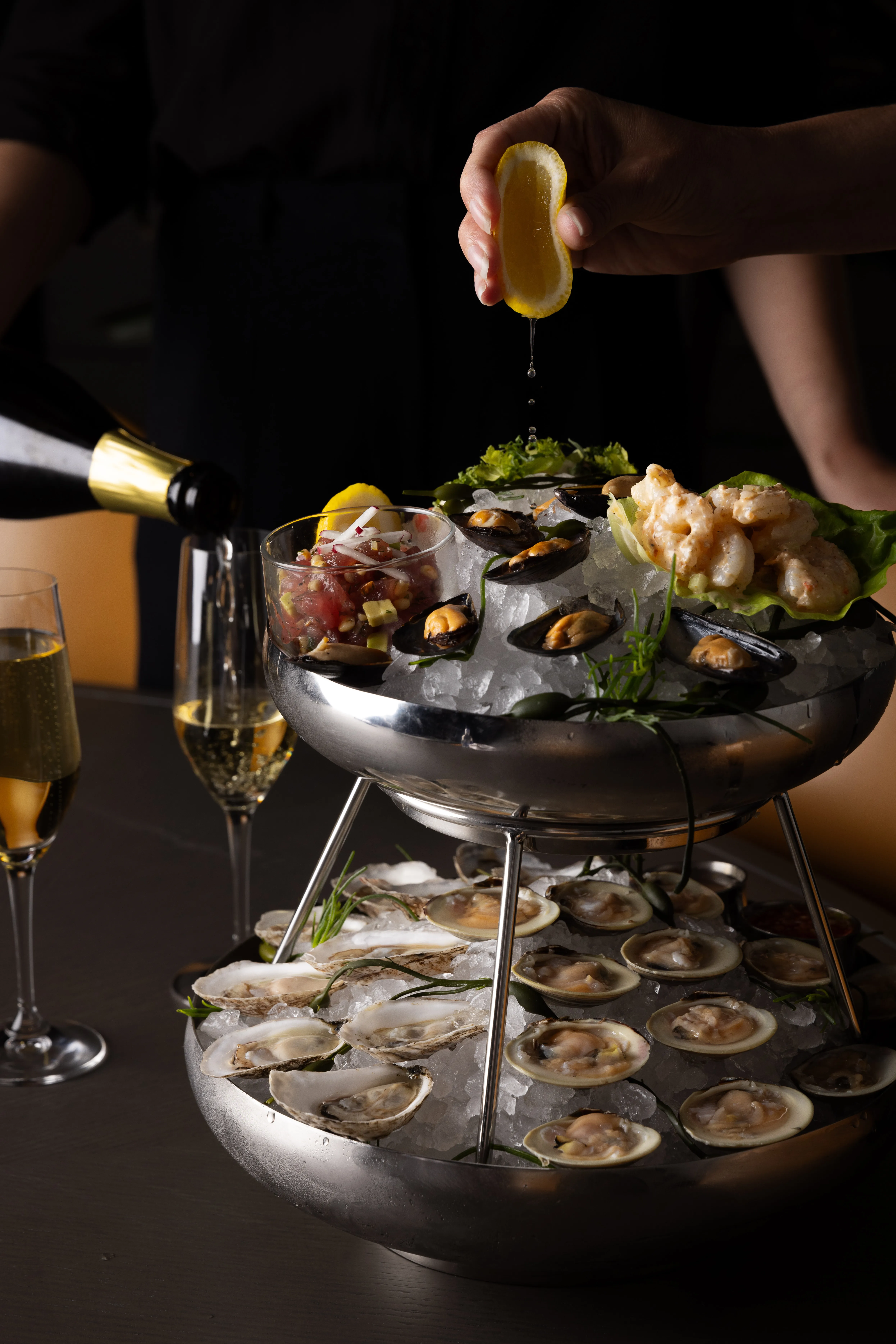 Two people toasting with cocktails over a table set with gourmet sandwiches and appetizers at The Vermilion Club.