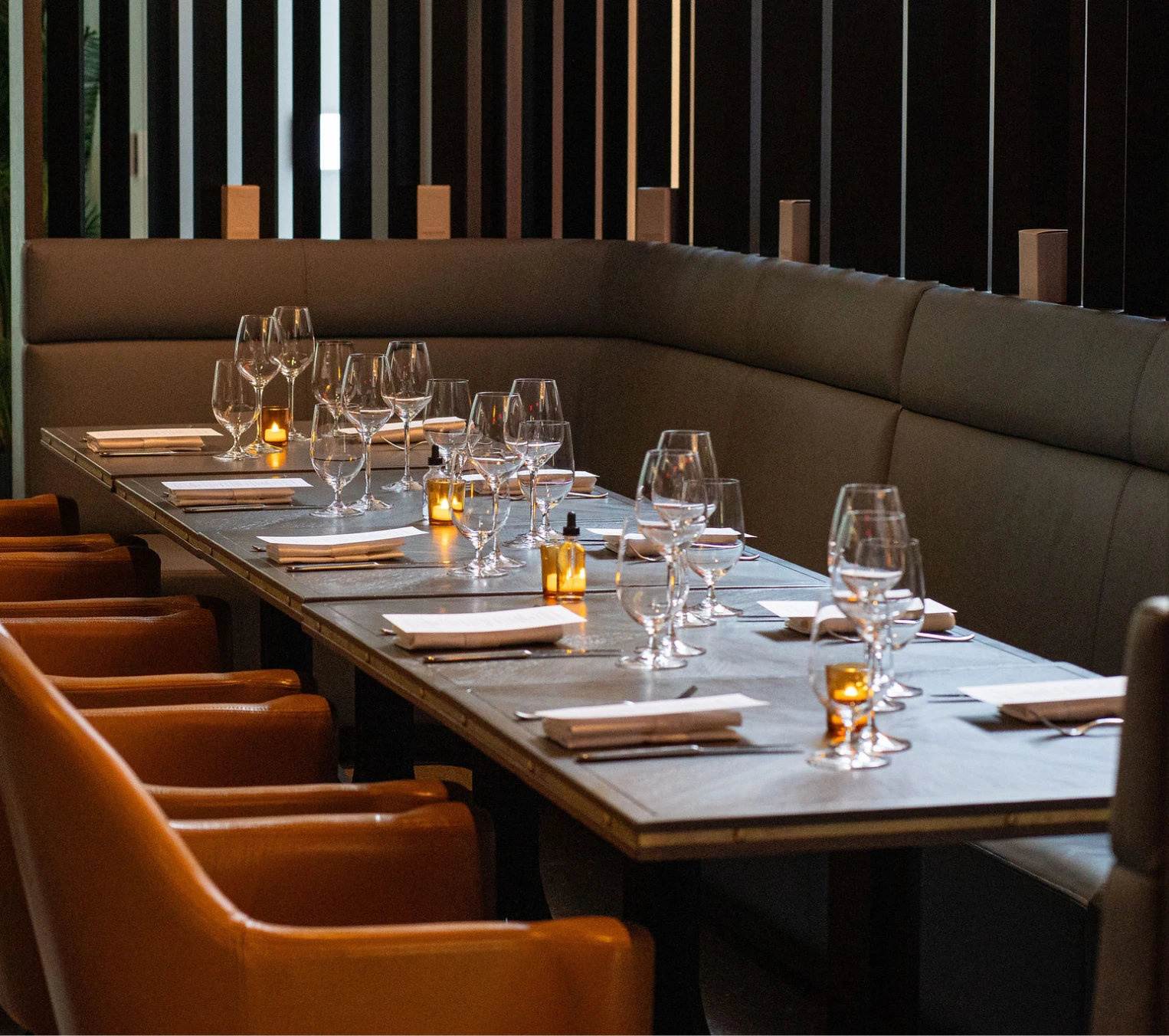 Private dining room at The Vermilion Club, featuring a rectangular table with cutttlery, glasses, and warm amber lighting, with a red glass sculpture and bar area in the background.