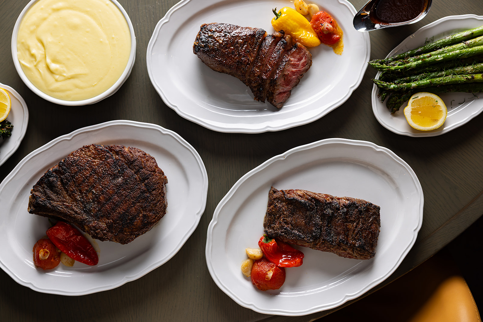 Prime 850 dry-aged steaks plated with roasted peppers and garlic, alongside asparagus, mashed potatoes, and sauce.