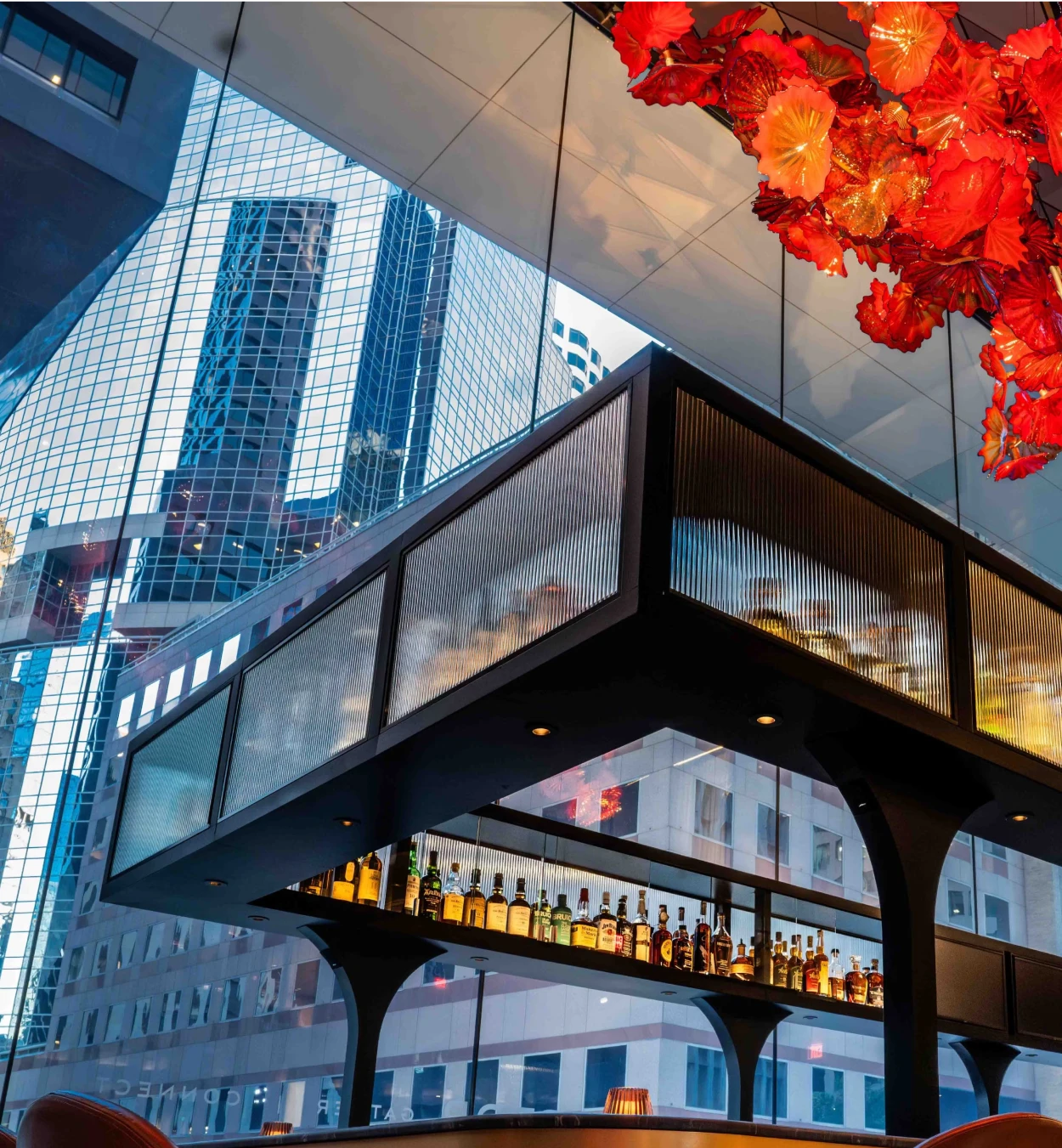 The Vermilion Club bar beneath the Chihuly sculpture with city reflections.