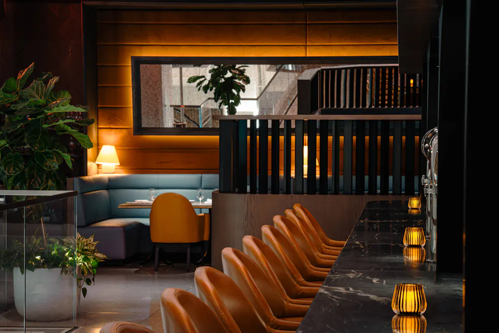 Marble bar with tan leather stools and warm candles beside cozy booth seating in Vermilion, one of the hidden gems in Boston.