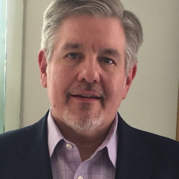 a man wearing a suit and tie smiling and looking at the camera