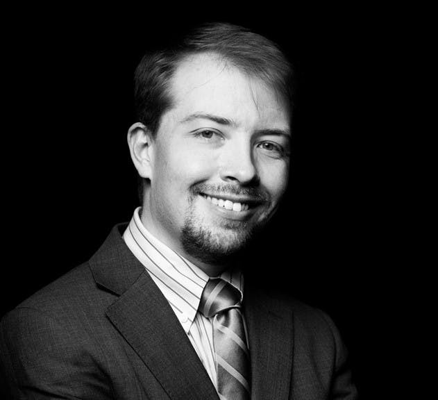 a man wearing a suit and tie smiling and looking at the camera