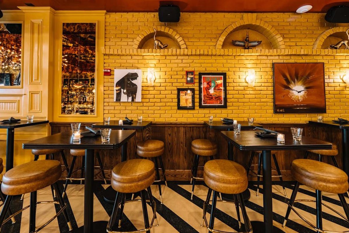 Trendy eatery with modern decor, including high-top tables, cushioned stools, and vibrant yellow wall accents