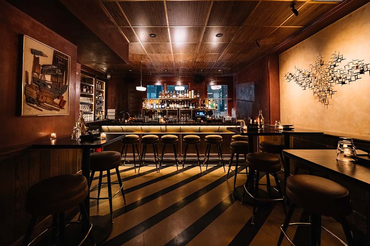 Rustic-chic bar setup with velvet and leather stools, low lighting, and a well-stocked back bar area