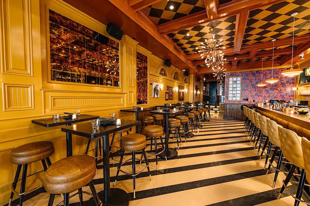 Cozy restaurant interior with yellow brick walls, framed artwork, and high tables surrounded by brown leather stools
