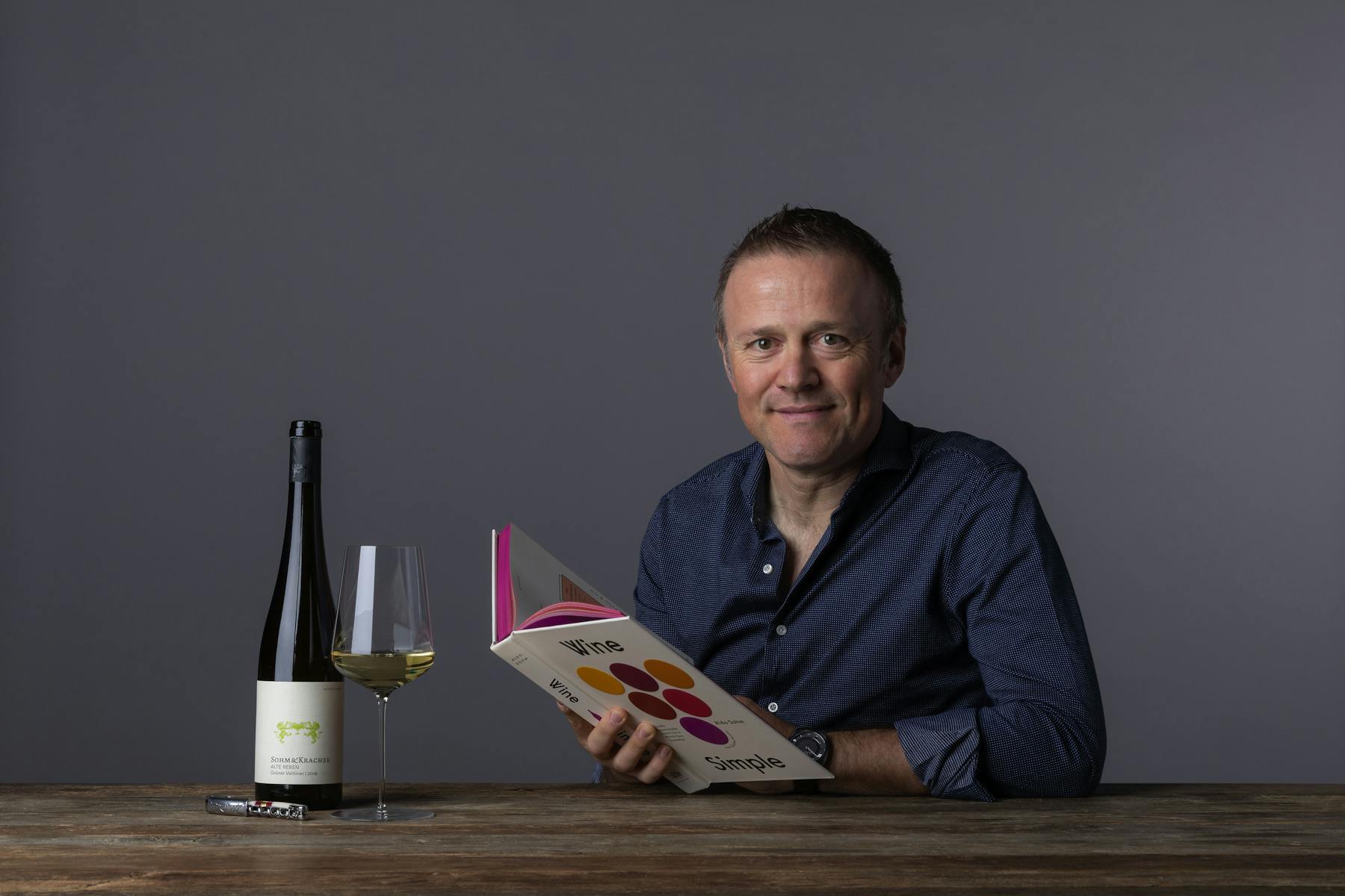 a man sitting at a table with a laptop and smiling at the camera