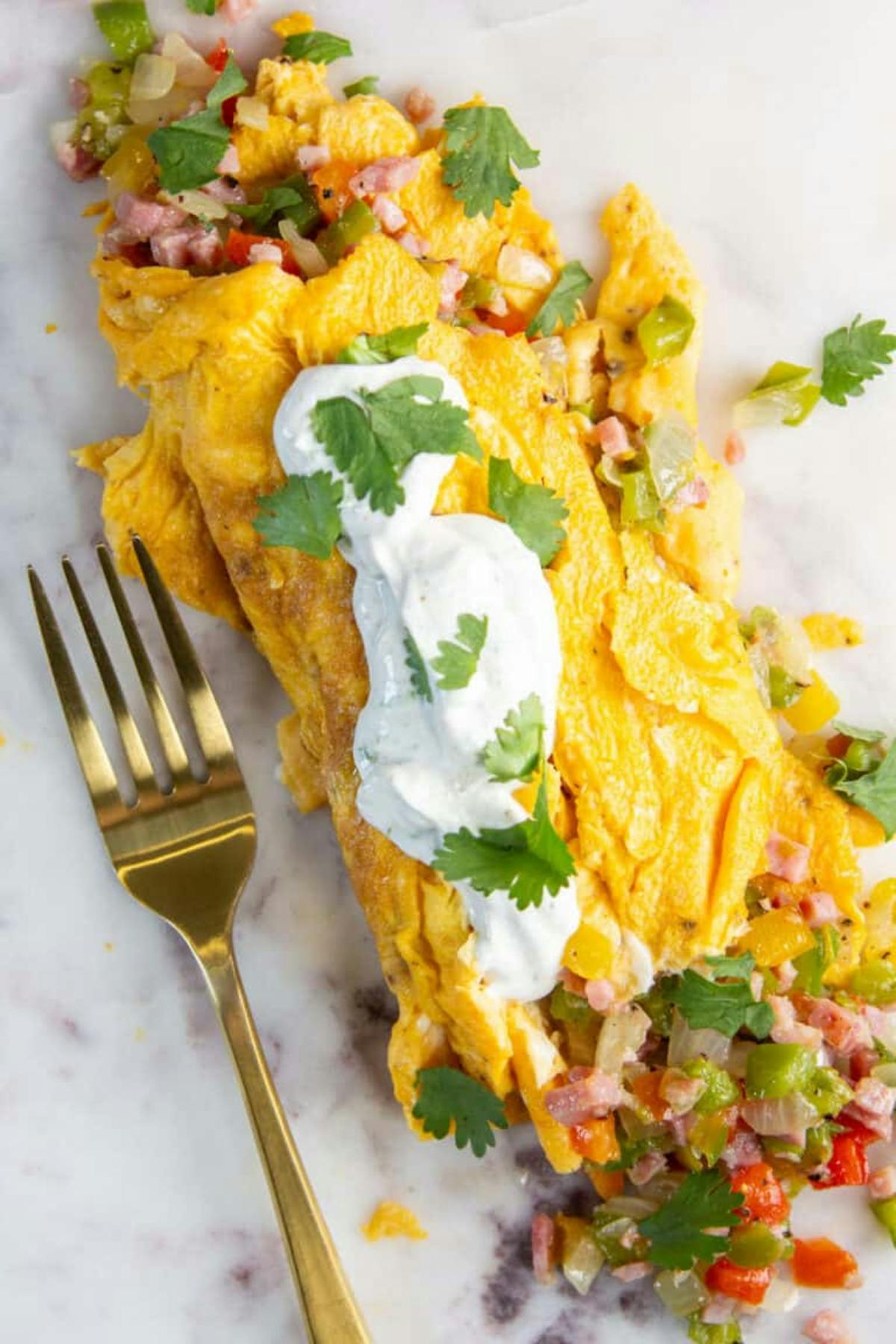 A plate of eggs and ham enchiladas topped with cheese and garnished with fresh herbs