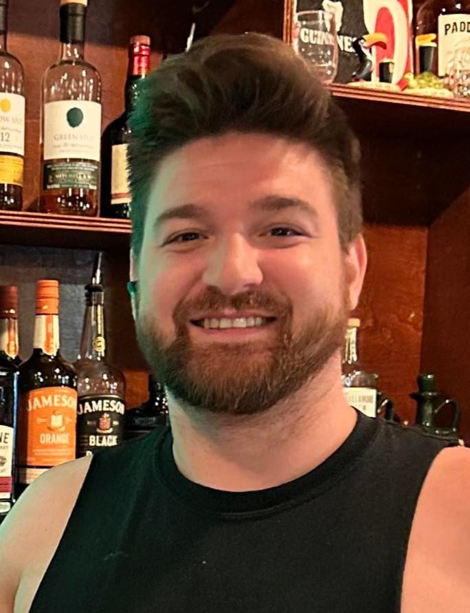 a man sitting at a table with wine glasses and smiling at the camera