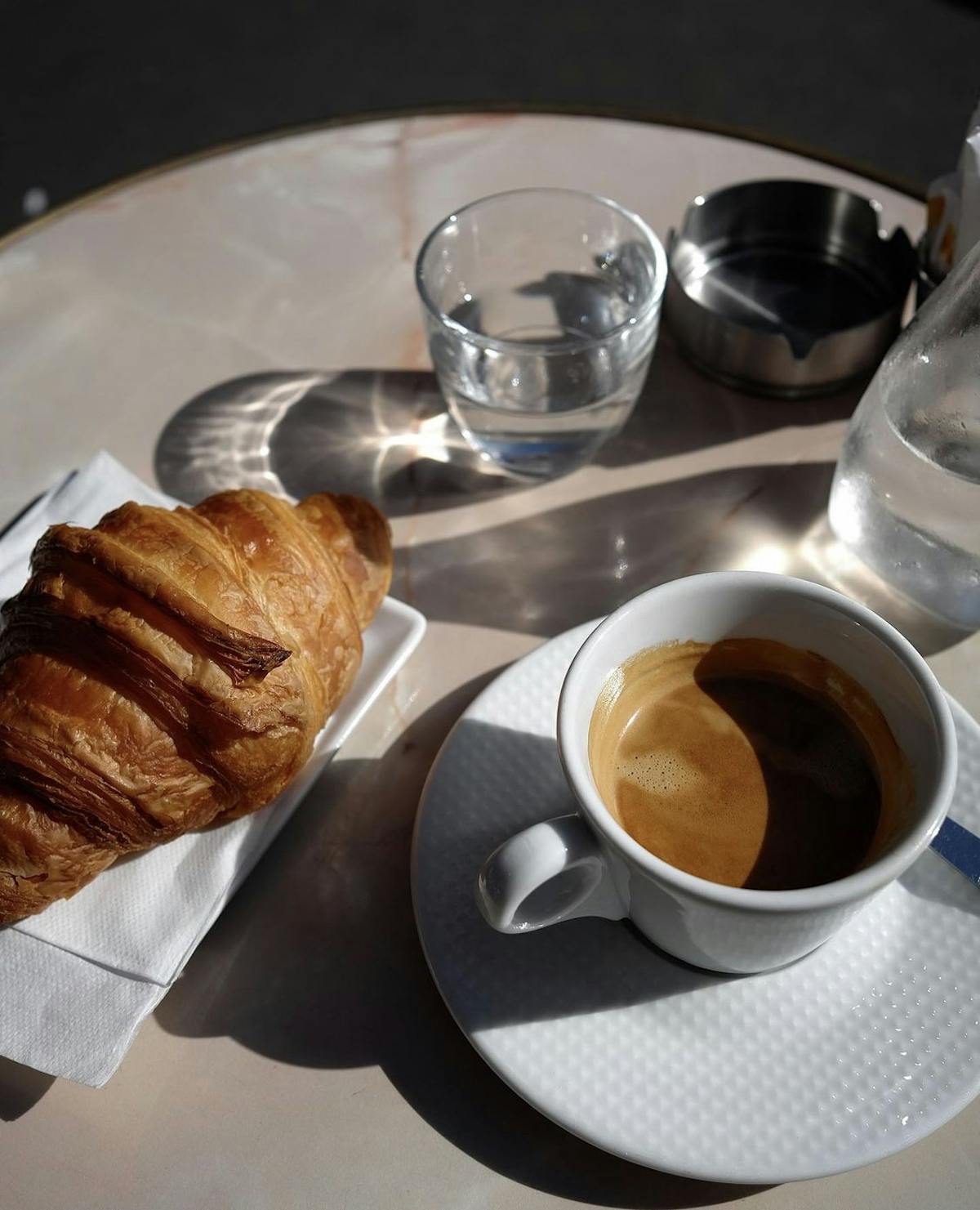 a cup of coffee and a croissanton a table