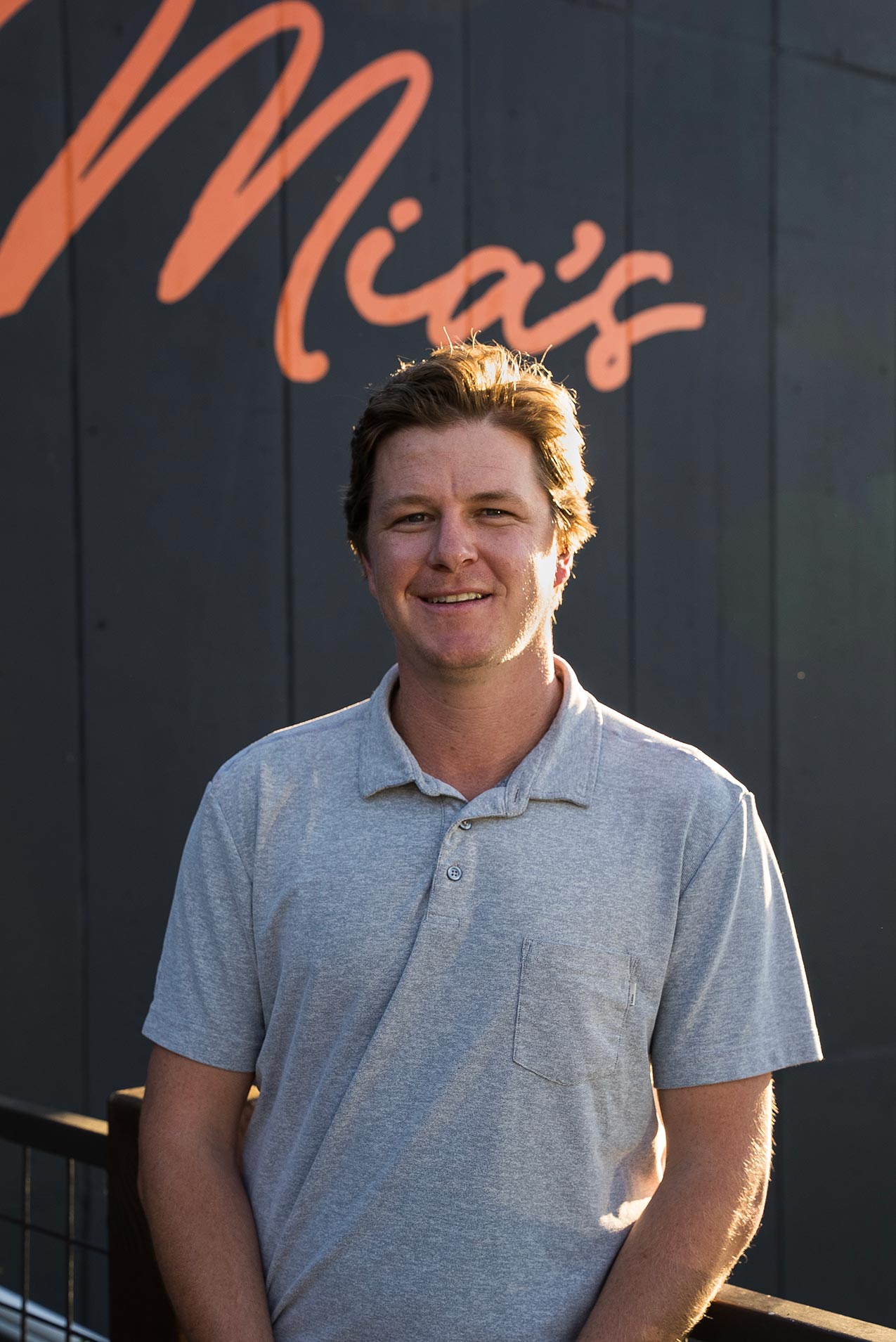 Manager Henry Staunton standing in front of a black panel wall, with partial view of orange Mia's logo in the top left.