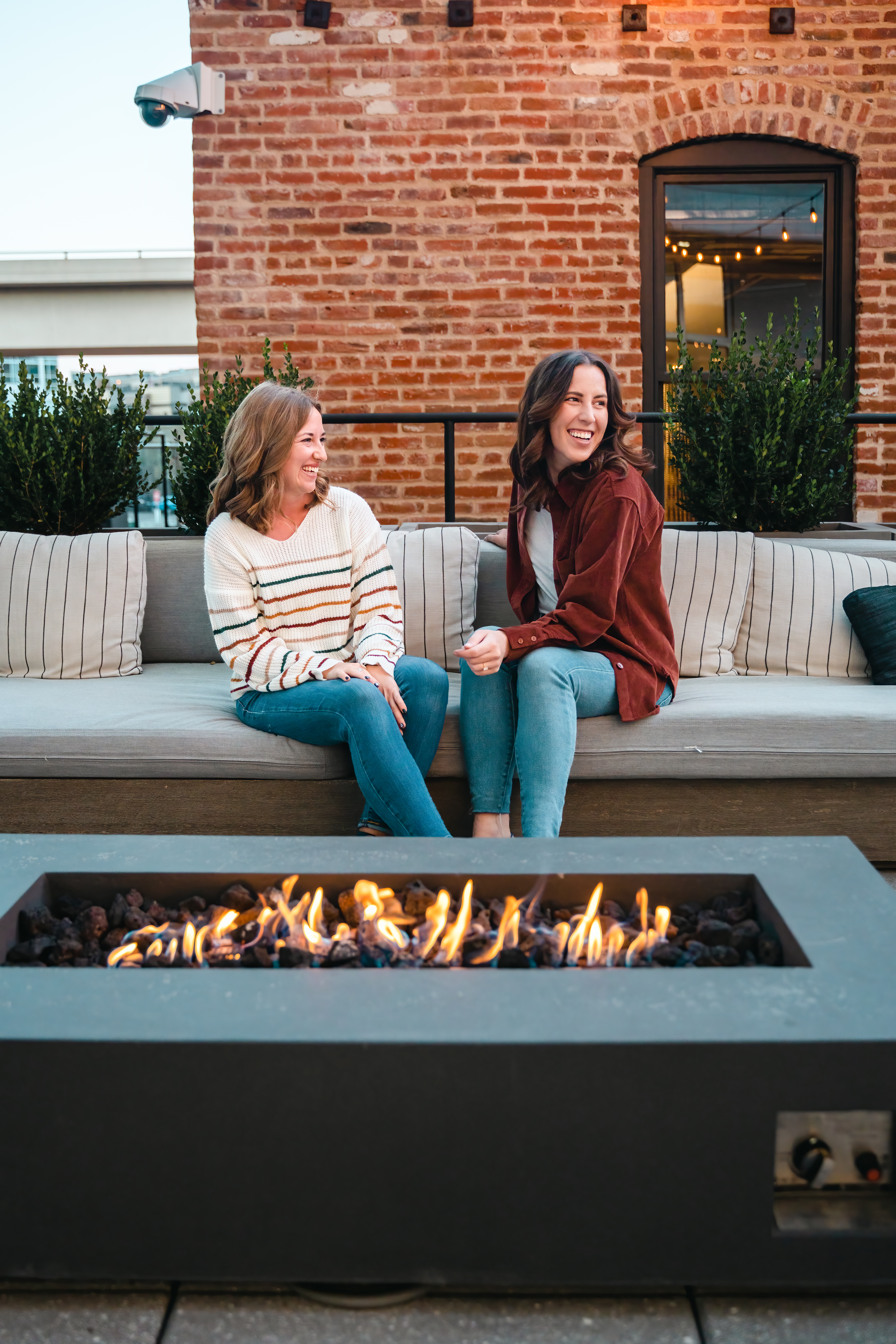two women sitting on a couch by the fire outside