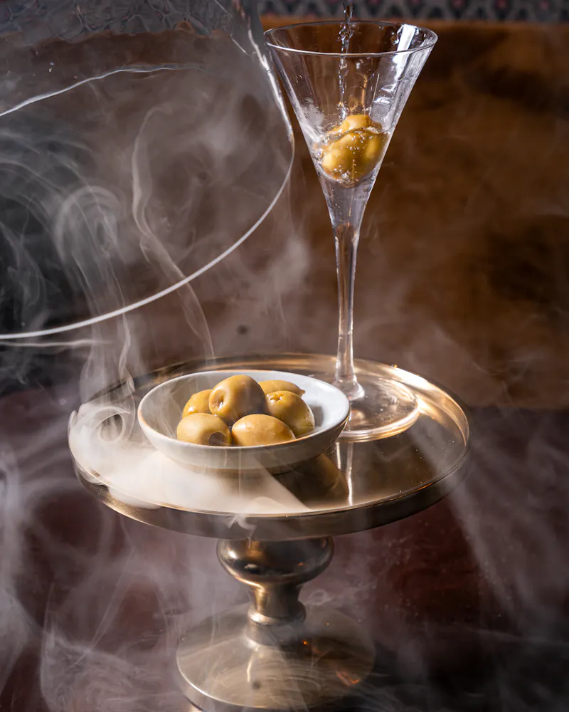 a bowl of olives and a martini glass with smoke