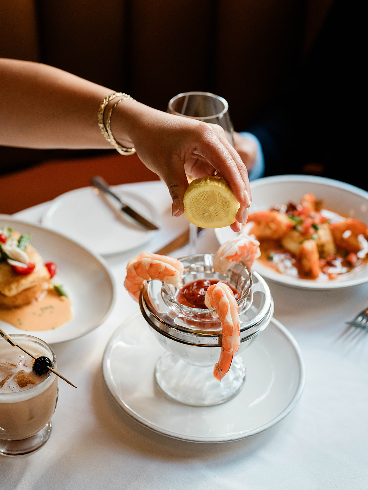 a hand spraying lemon on a jumbo shrimp dish
