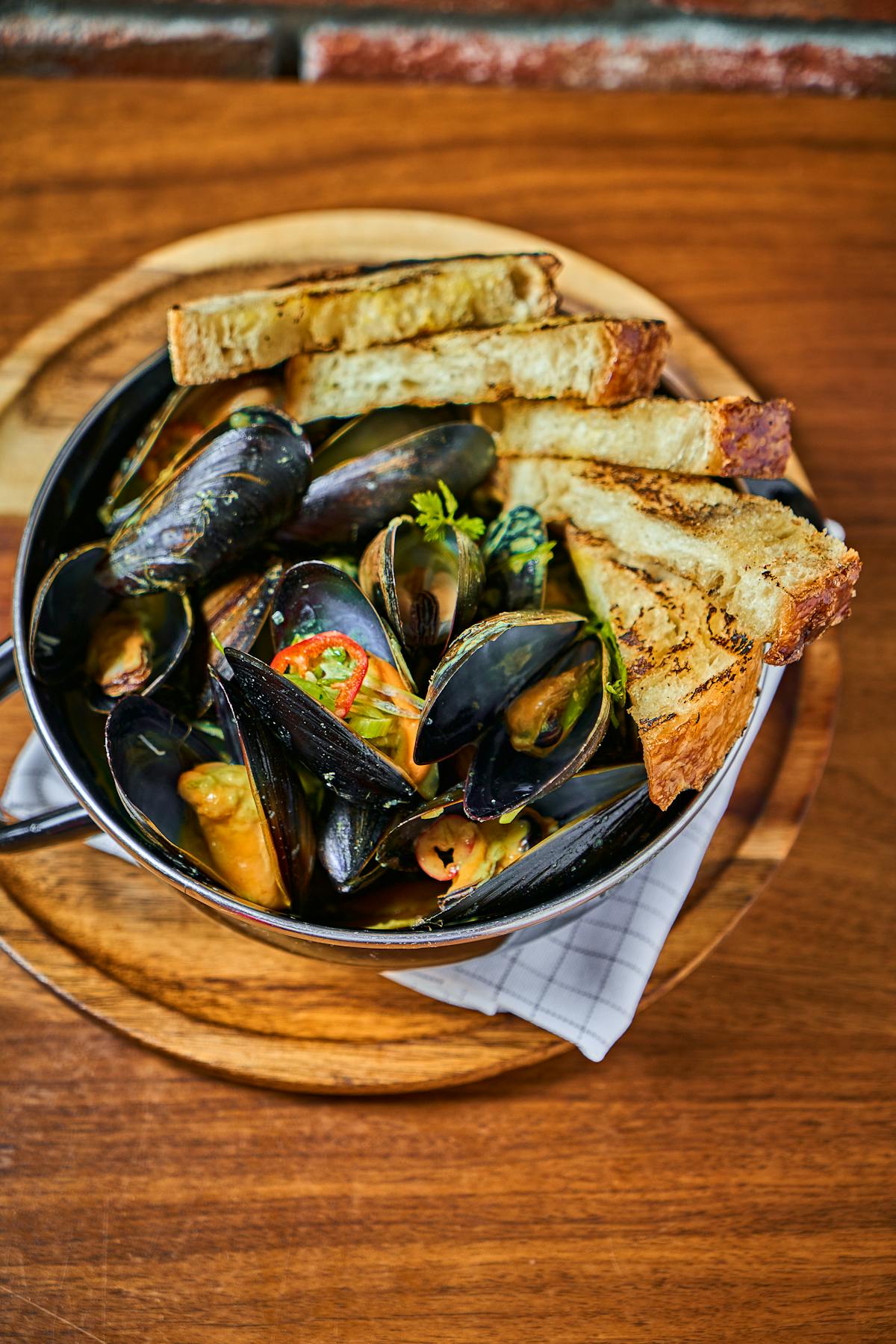 bowl of mussels garnished with peppers and a side of grilled bread 