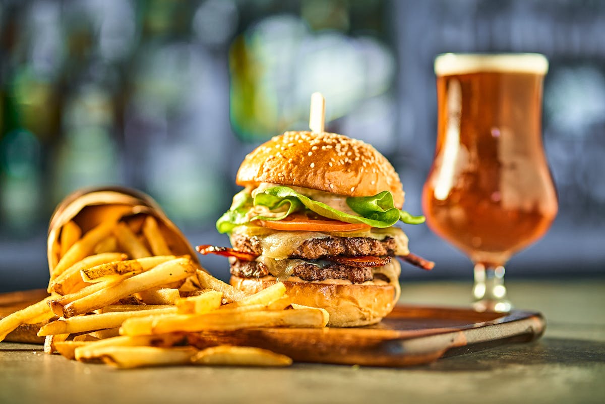 close up of a double cheeseburger with french fries and a craft beer