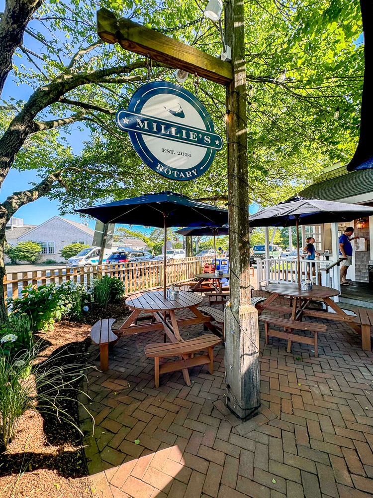 a patio under a tree with picnic tables and umbrellas