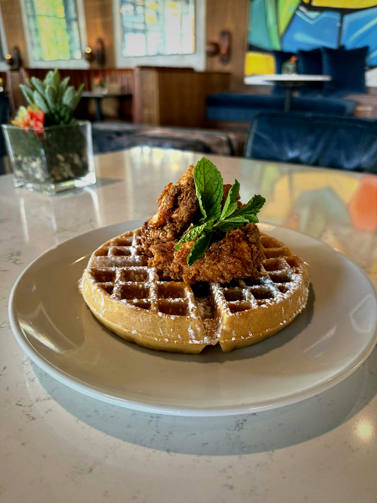 a waffle with chicken and mint leaves on a white plate