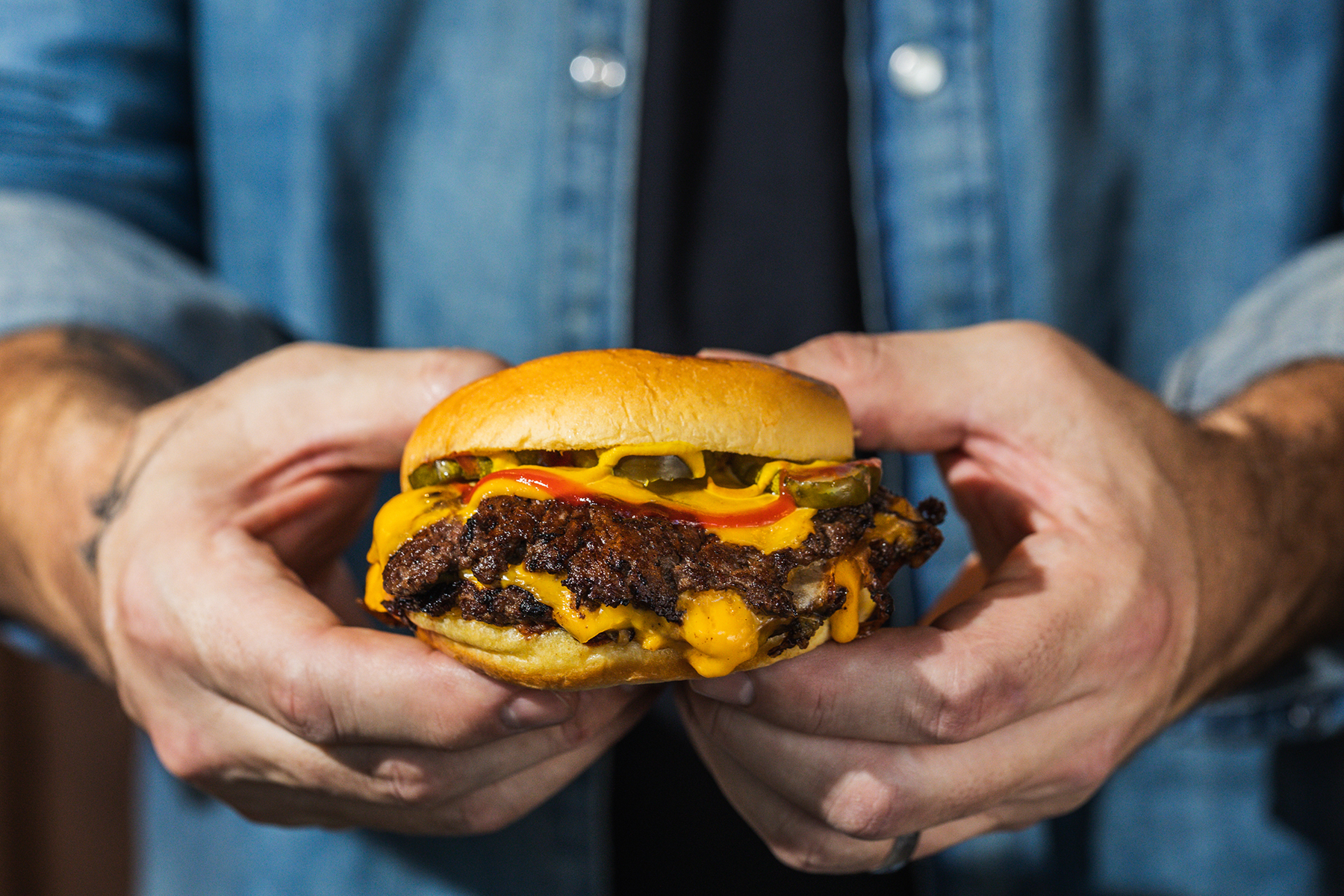 A Gotham Burger Social Club smash burger held in both hands