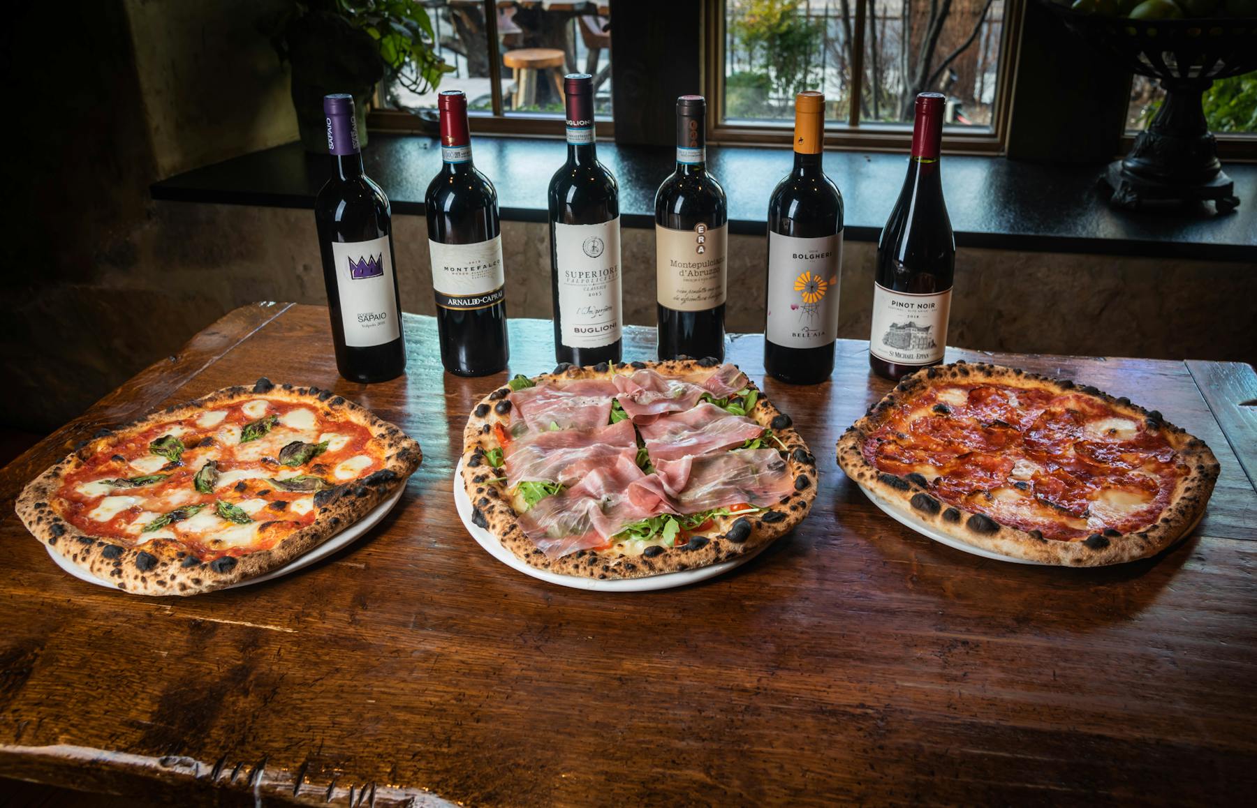 a pizza sitting on top of a table next to a bottle of wine
