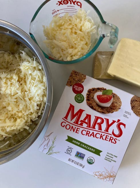 a box of crackers next to two bowls of shredded cheese