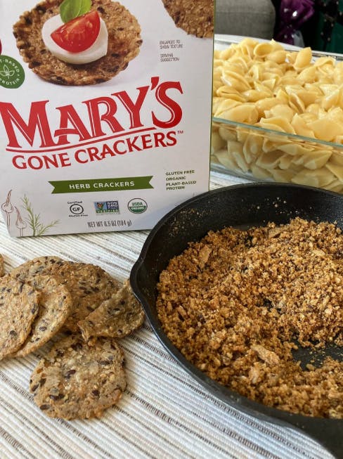 a box of crackers next to a cast iron skillet with crumbled crackers and a pan of pasta