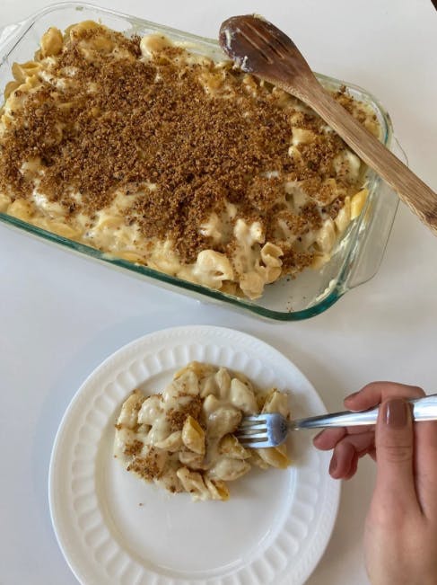 a serving of mac and cheese being eaten with a fork next to a casserole dish of mac and cheese