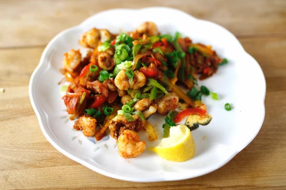 a white plate with shrimp, peppers, and green onion with a lemon wedge
