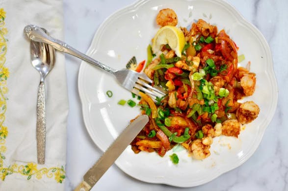 shrimp and peppers on a white plate with a fork and knife