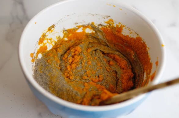 a bowl of pancake batter with pumpkin puree being stirred in